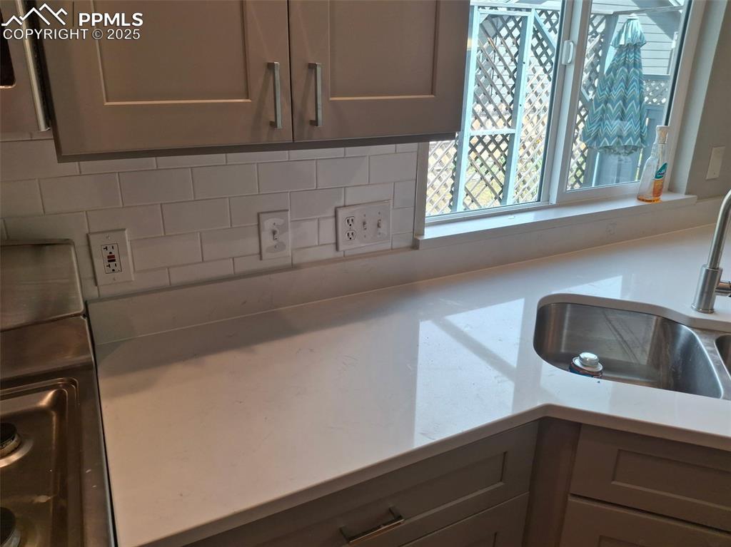 Image 8 of 45: Kitchen featuring light countertops, gray cabinetry, and decorative tile ba