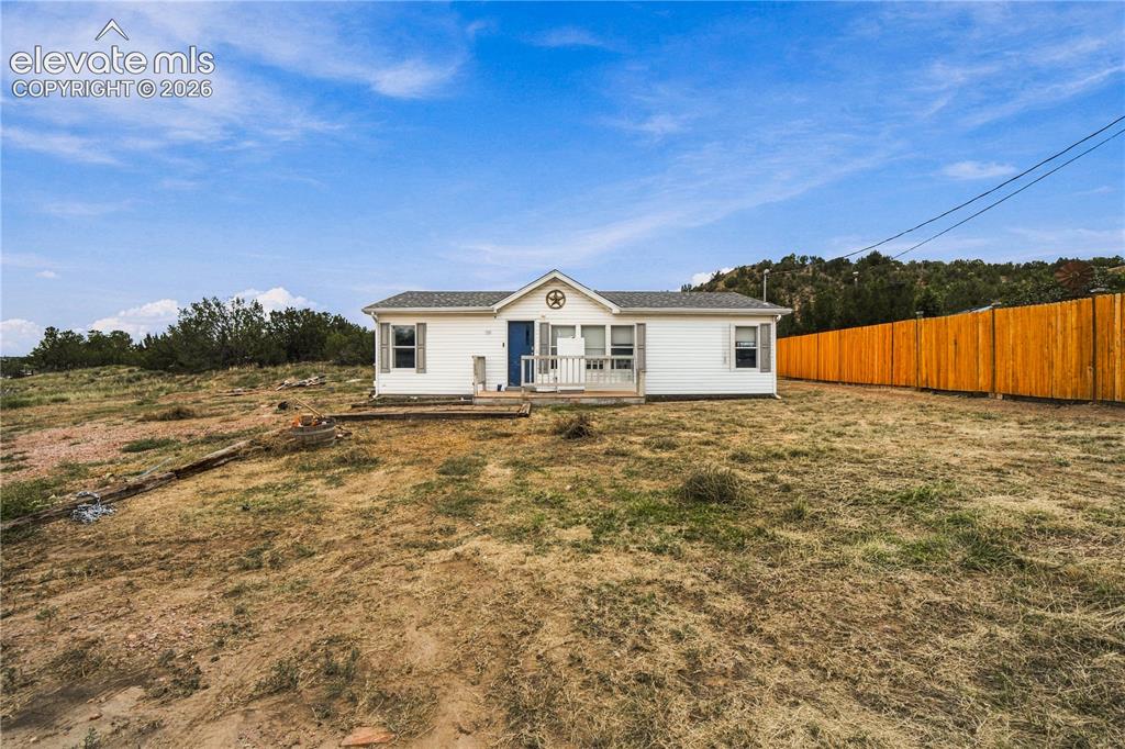 Caption: White exterior siding with a blue entry door, a covered porch, and a wood privacy fence