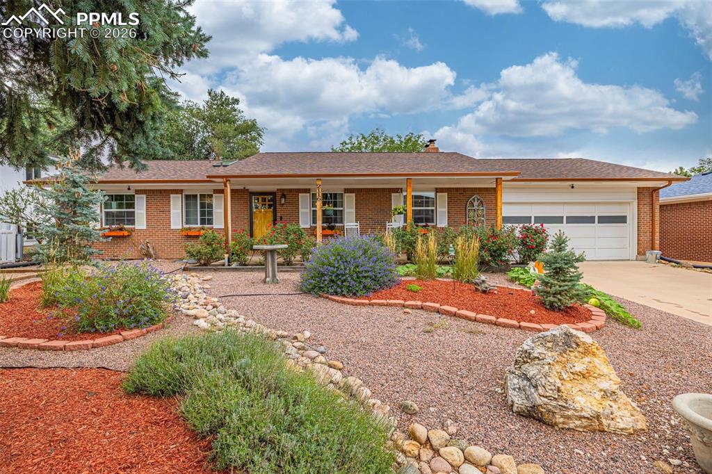 Caption: Ranch-style home with a chimney, brick siding, a porch, and a garage