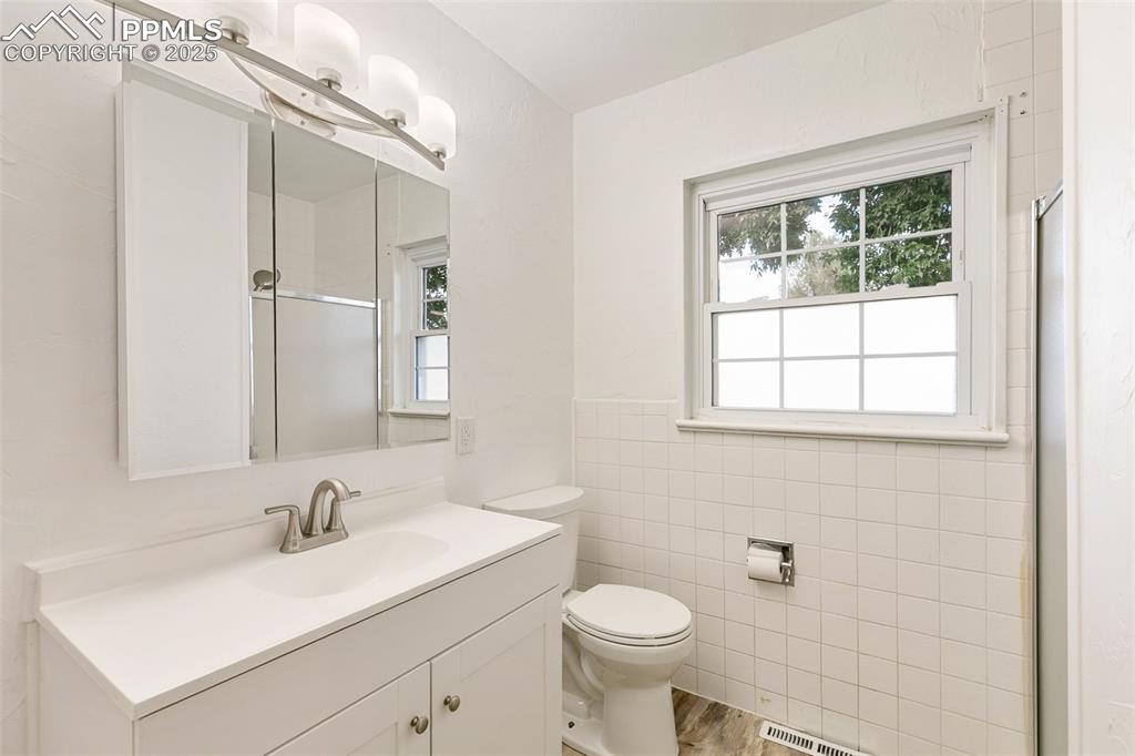 Image 12 of 17: Full bath with a stall shower, vanity, tile walls, and wood finished floors