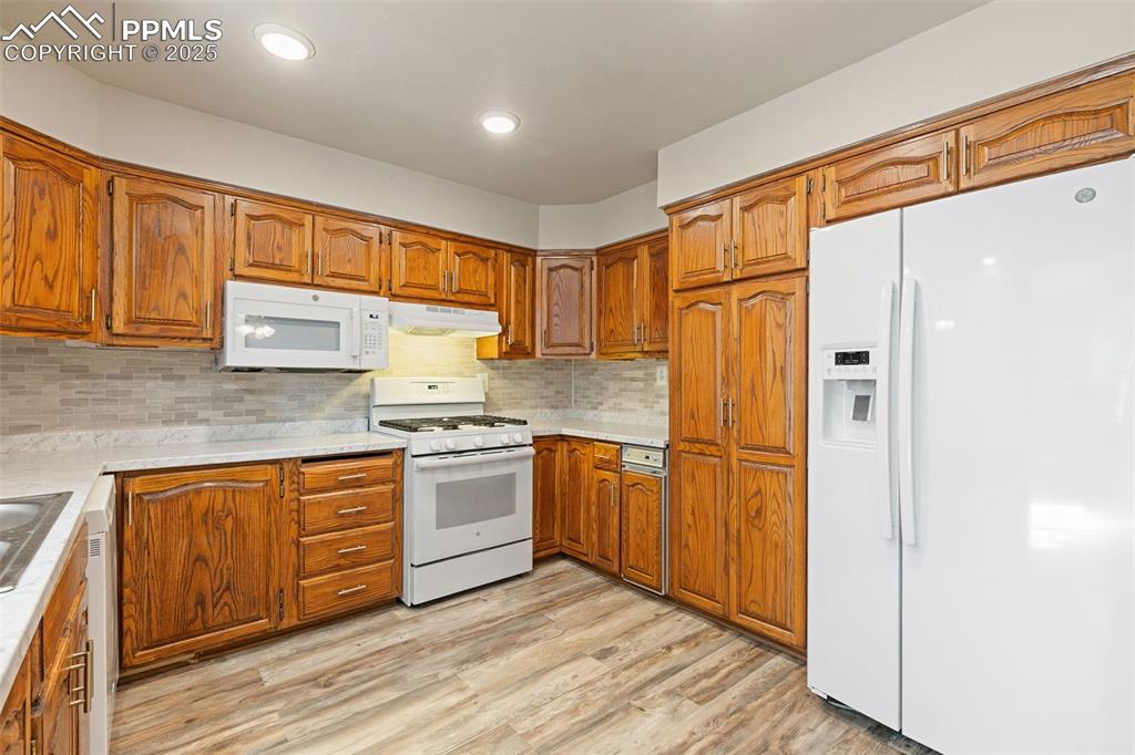 Image 5 of 17: Kitchen featuring white appliances, light countertops, brown cabinetry, lig