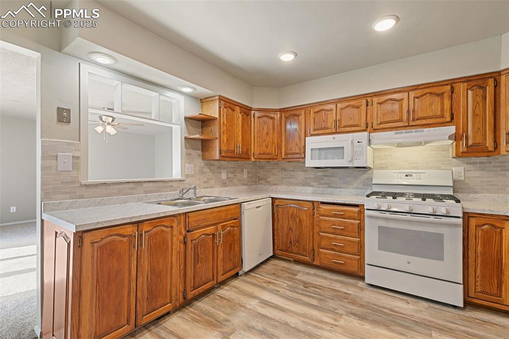 Image 6 of 17: Kitchen with white appliances, tasteful backsplash, brown cabinets, under c