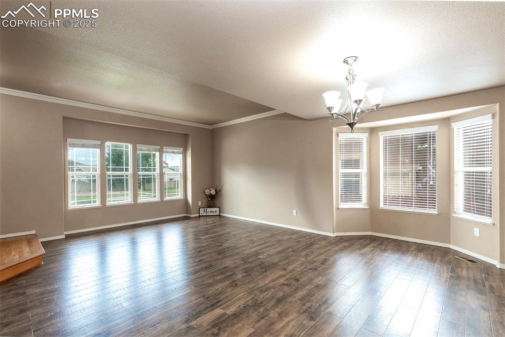 Image 3 of 46: Unfurnished room with a chandelier, crown molding, dark wood-type flooring,
