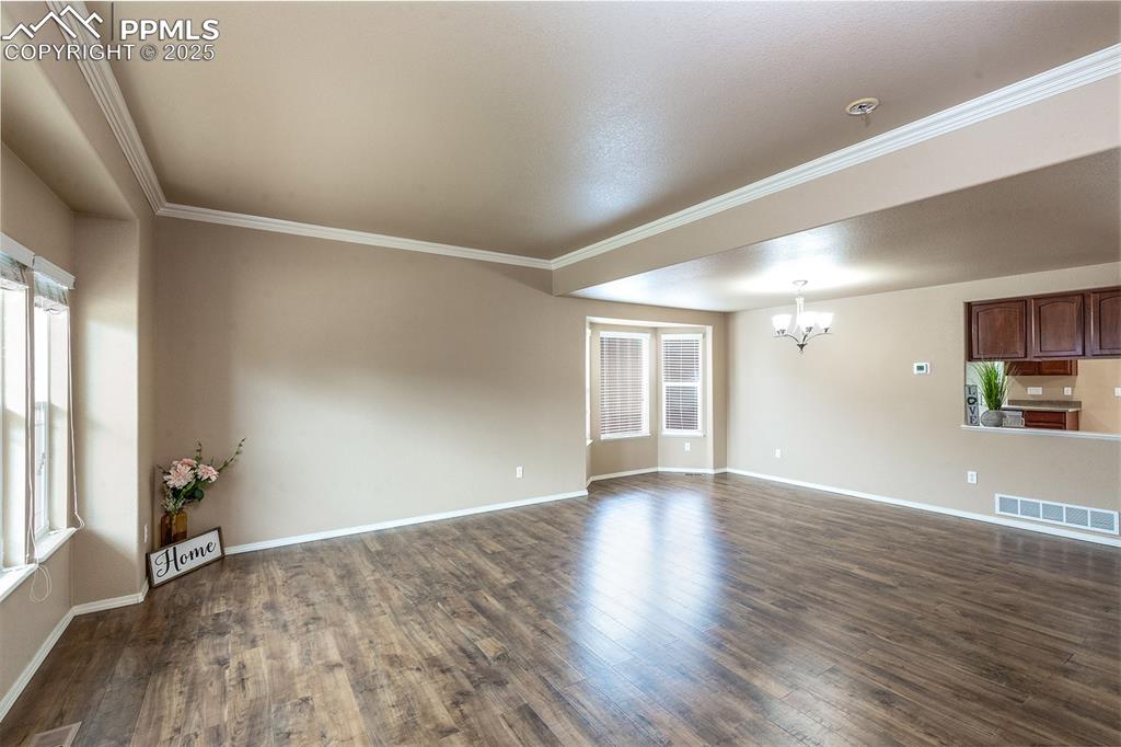 Image 4 of 46: Unfurnished room featuring a chandelier, dark wood-style floors, crown mold