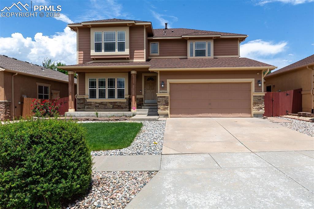 Image 46 of 46: View of front of house featuring driveway, stone siding, an attached garage