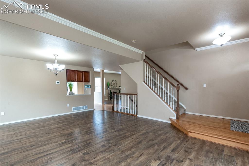 Image 6 of 46: Unfurnished living room with dark wood finished floors, a chandelier, stair