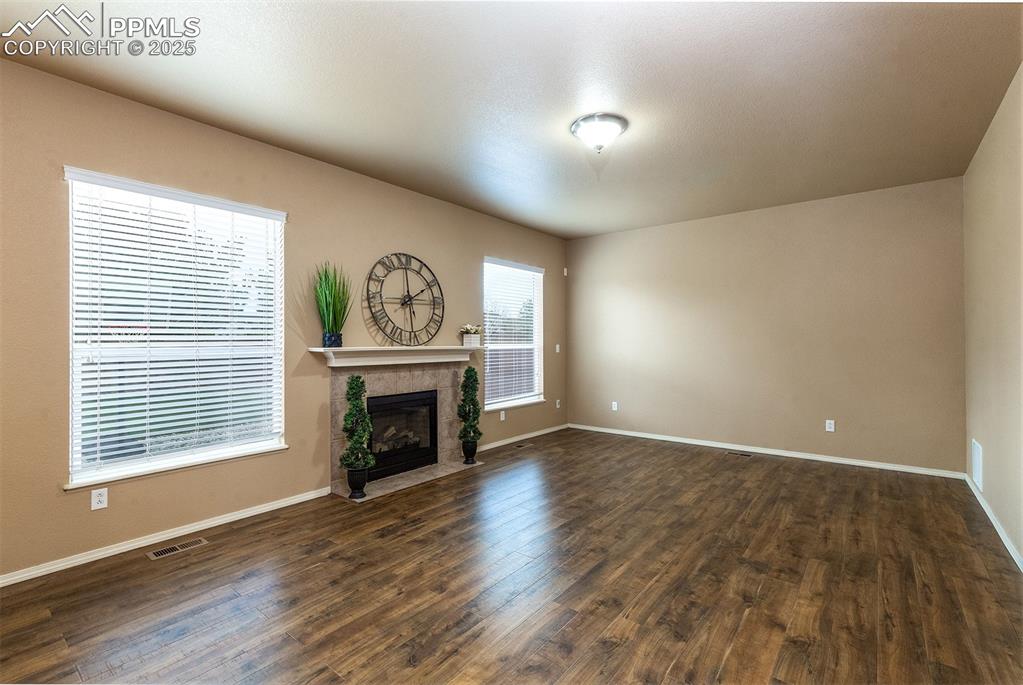 Image 7 of 46: Unfurnished living room with dark wood-style floors and a tile fireplace