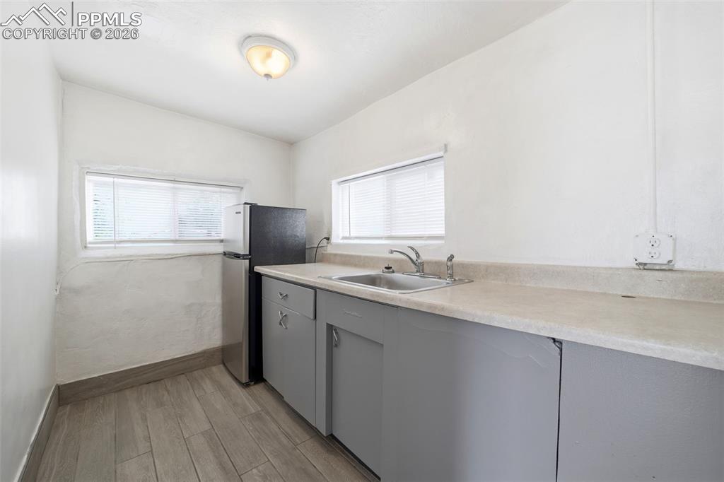 Image 13 of 50: Compact kitchen space featuring wood-finish flooring, two windows with blin