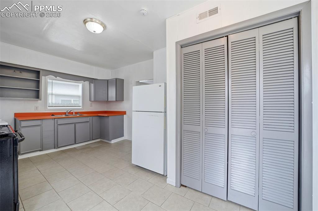 Image 15 of 50: Kitchen featuring light gray cabinetry, vibrant orange countertops, and a s