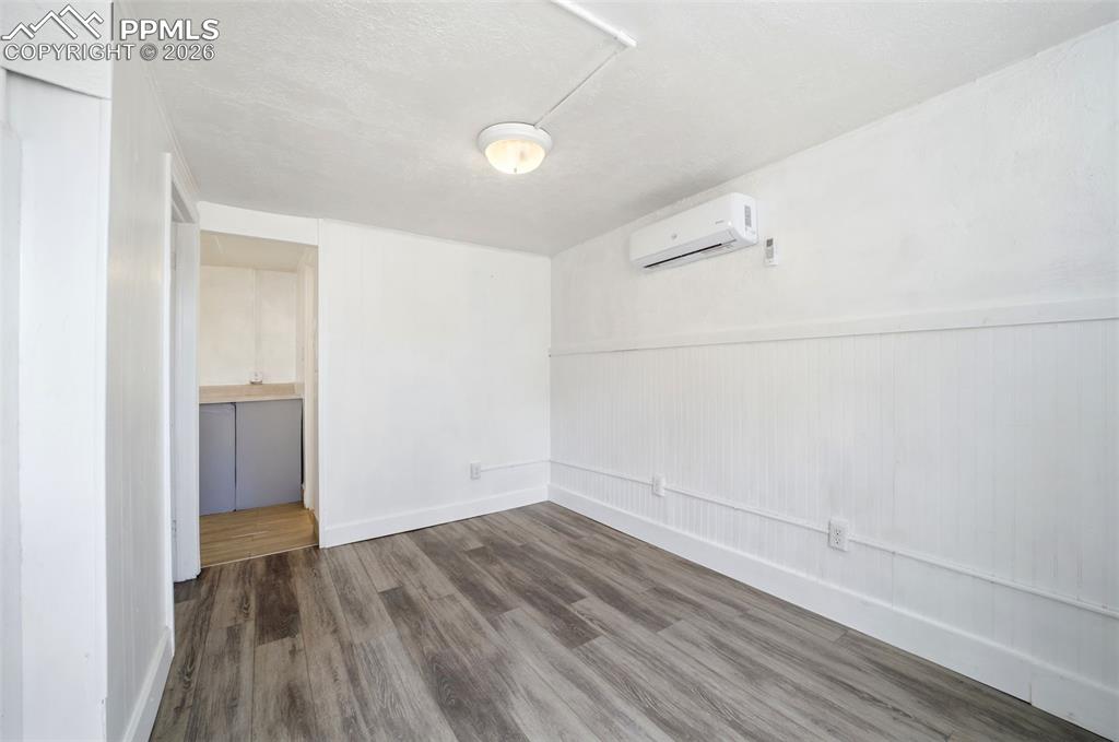 Image 3 of 50: Room with wood-finish flooring, white walls, and a white beadboard wainscot