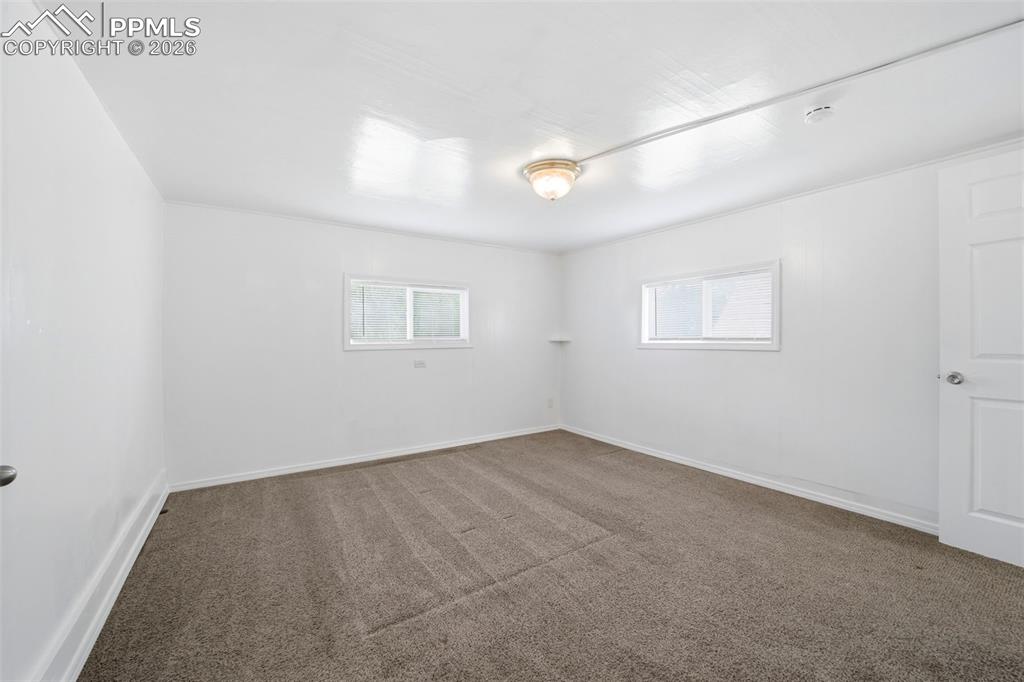 Image 35 of 50: Spacious room featuring neutral carpeting, white paneled walls, and two win