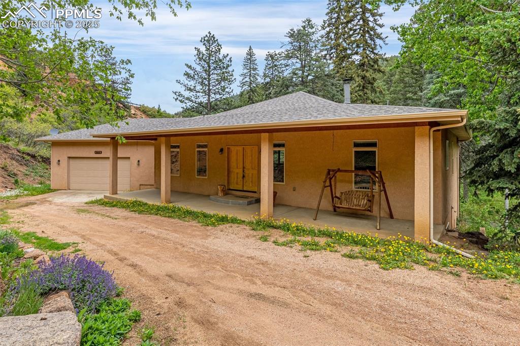 Caption: View of front of property with stucco siding, a garage, driveway, and a shingled roof