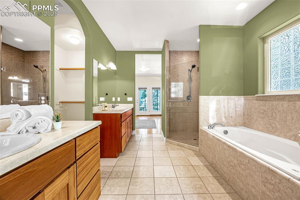 Image 14 of 41: Full bath featuring a shower stall, two vanities, a garden tub, and tile pa