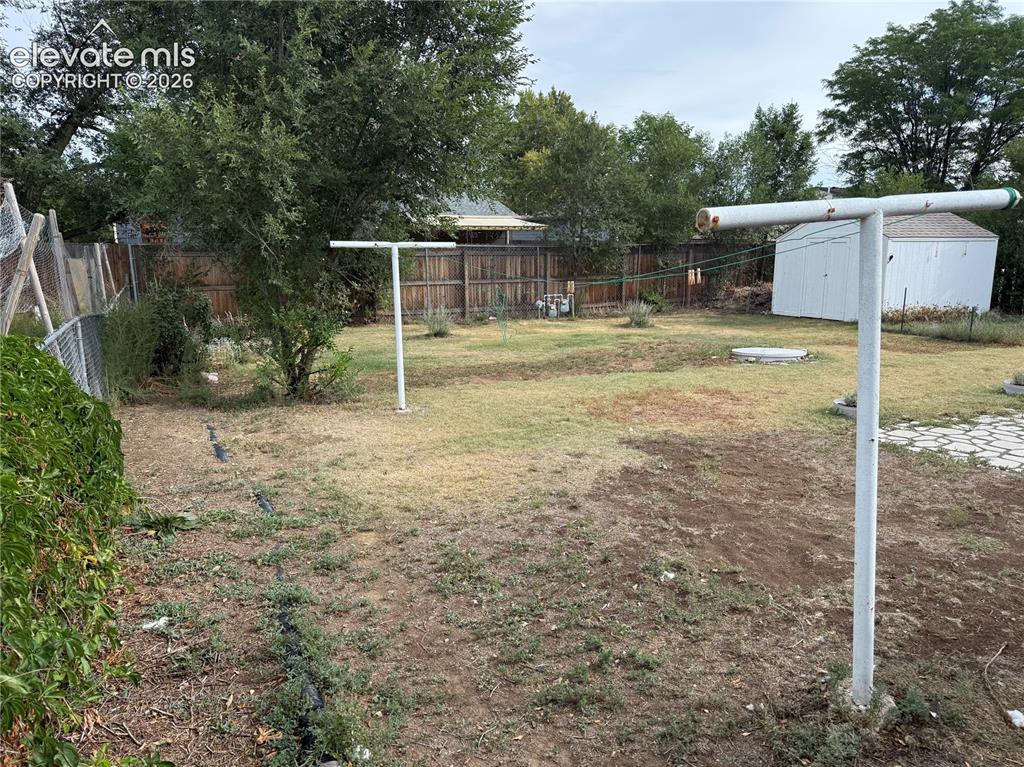 Image 16 of 16: Expansive backyard with a storage shed, mature trees, wood fence, and chain