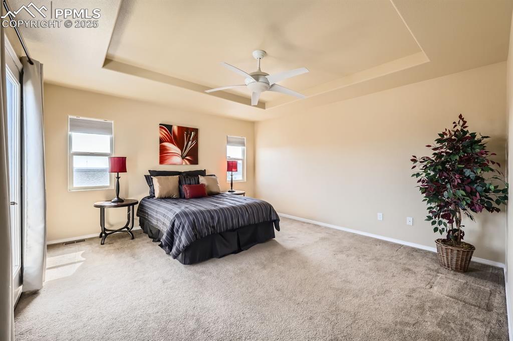 Image 17 of 34: Bedroom with a raised ceiling, baseboards, carpet flooring, and ceiling fan