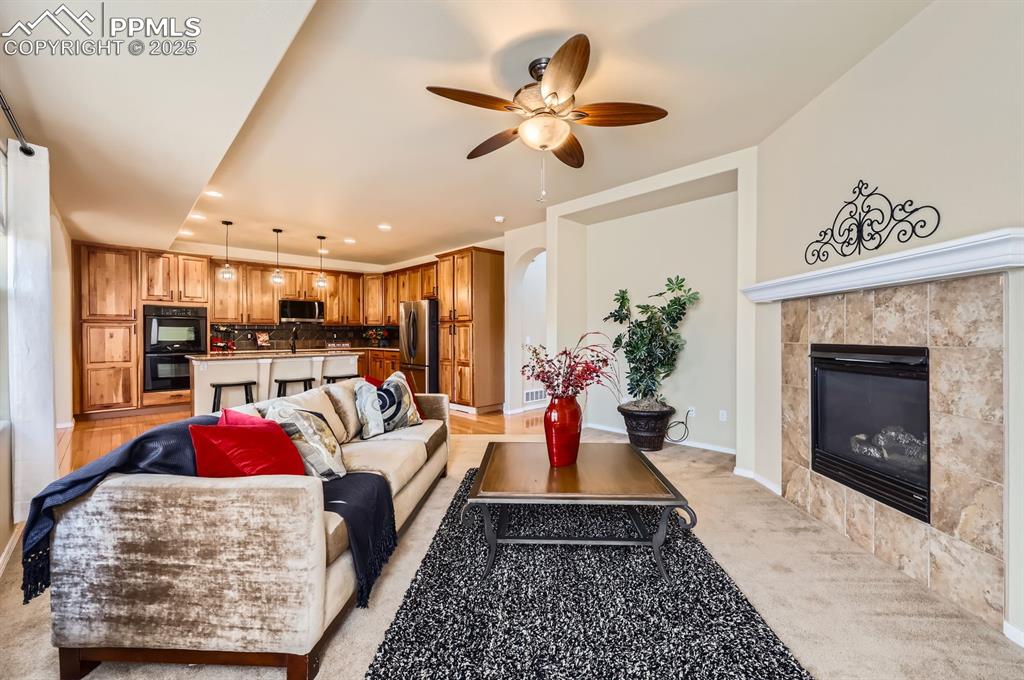 Image 5 of 34: Living room with a ceiling fan, a tile fireplace, light colored carpet, and