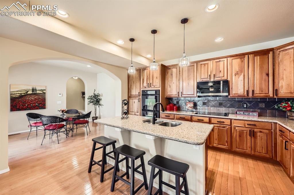 Image 6 of 34: Kitchen with a sink, black appliances, arched walkways, brown cabinetry, an