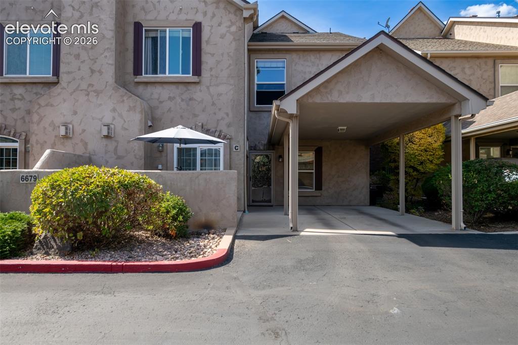 Caption: Welcoming covered carport entry with stucco exterior and mature landscaping