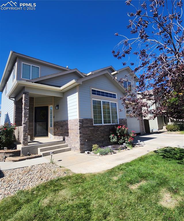 Caption: View of front facade with driveway, stone siding, a front yard, and a porch