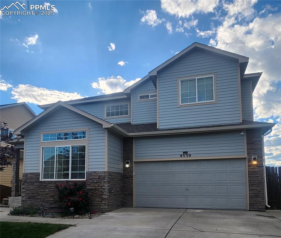 Image 2 of 45: View of front of house featuring stone siding, a garage, and concrete drive