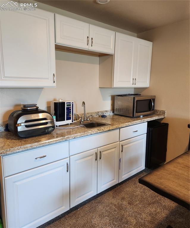 Image 28 of 45: Wet bar , kitchen with refrigerator in the basement cabinets, light stone c