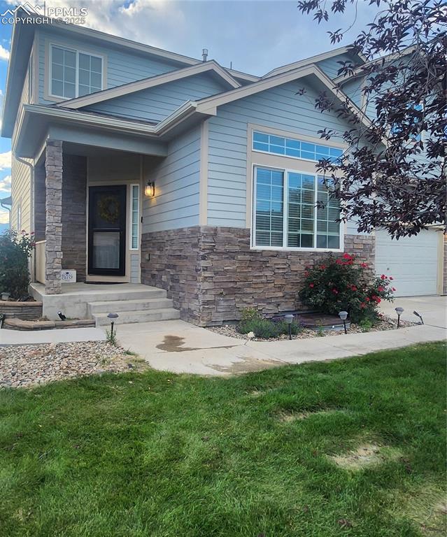 Image 4 of 45: View of front facade with stone siding, a garage, and a front lawn