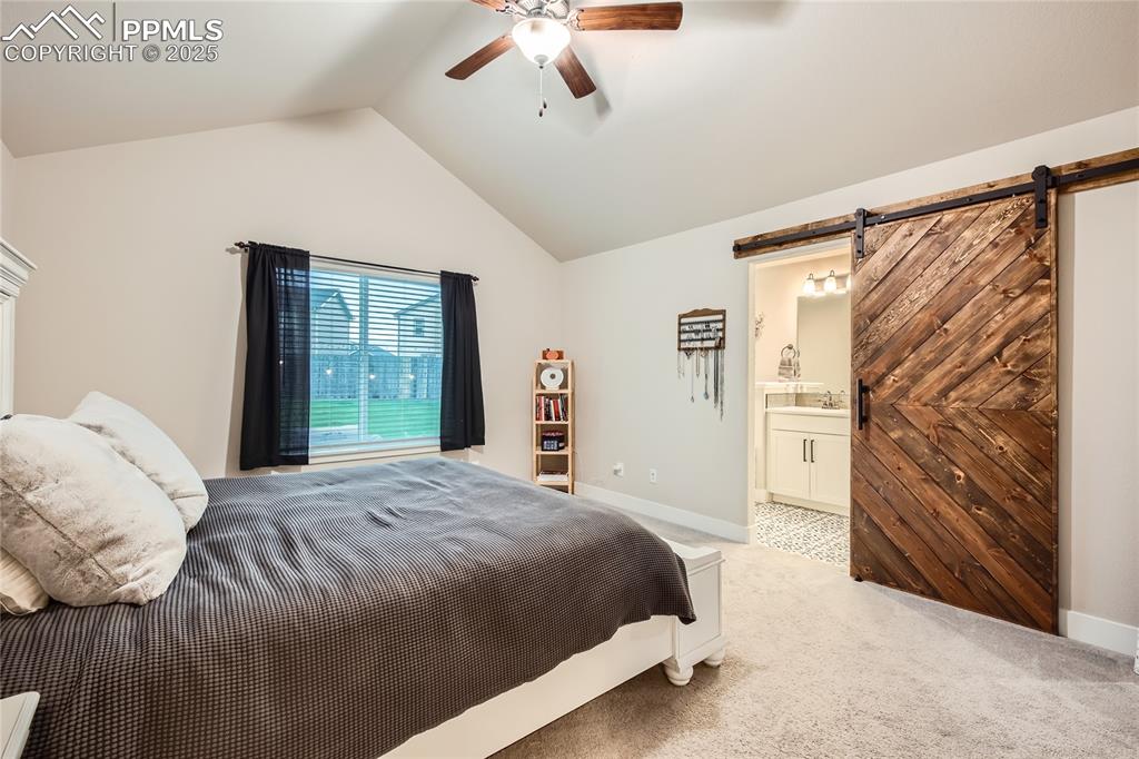 Image 12 of 37: Bedroom featuring a barn door, light carpet, lofted ceiling, ceiling fan, a