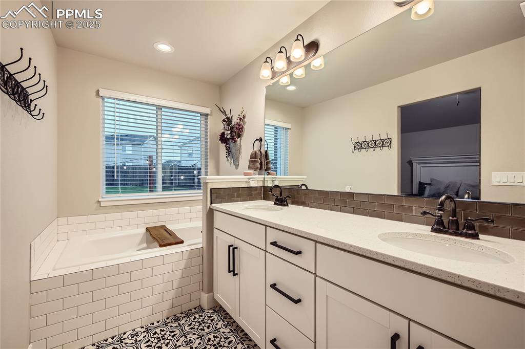 Image 14 of 37: Full bathroom with double vanity, a garden tub, backsplash, tile patterned