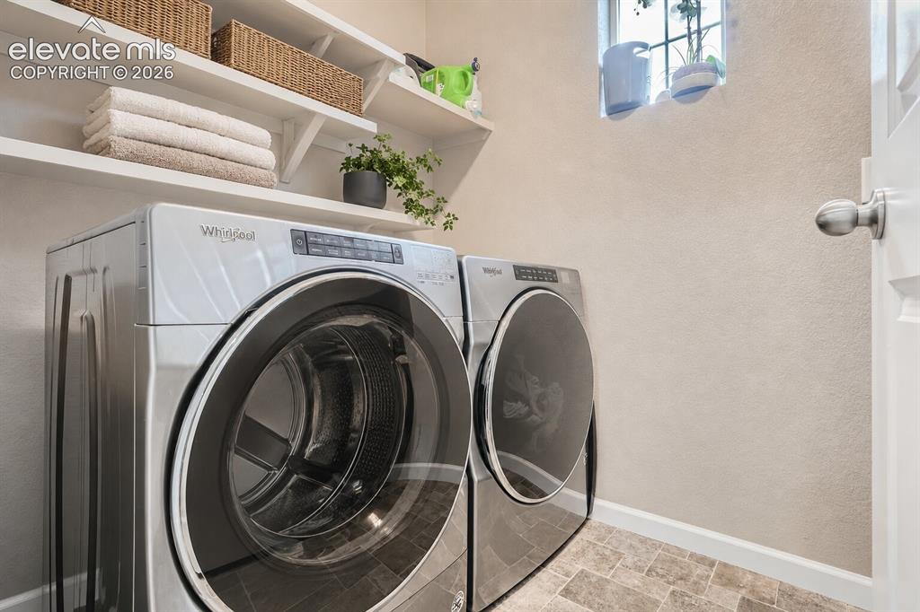 Image 25 of 35: Laundry space featuring built-in wall-mounted shelving and natural stone-fi