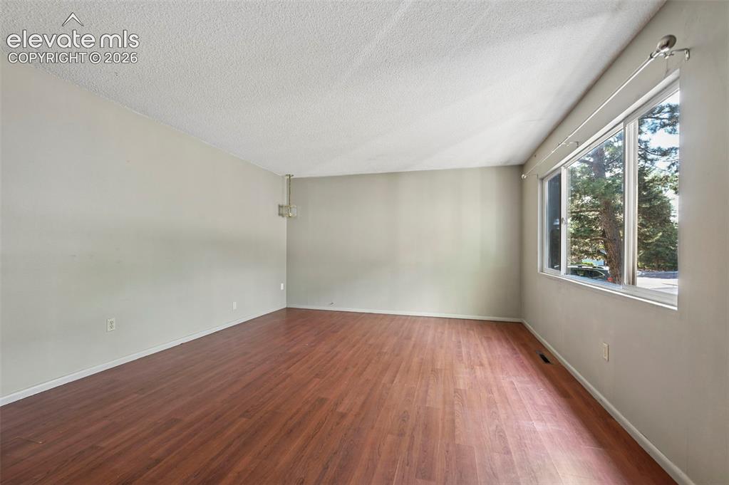 Image 14 of 32: Spacious room featuring wood-finish flooring, light-toned walls, and a text