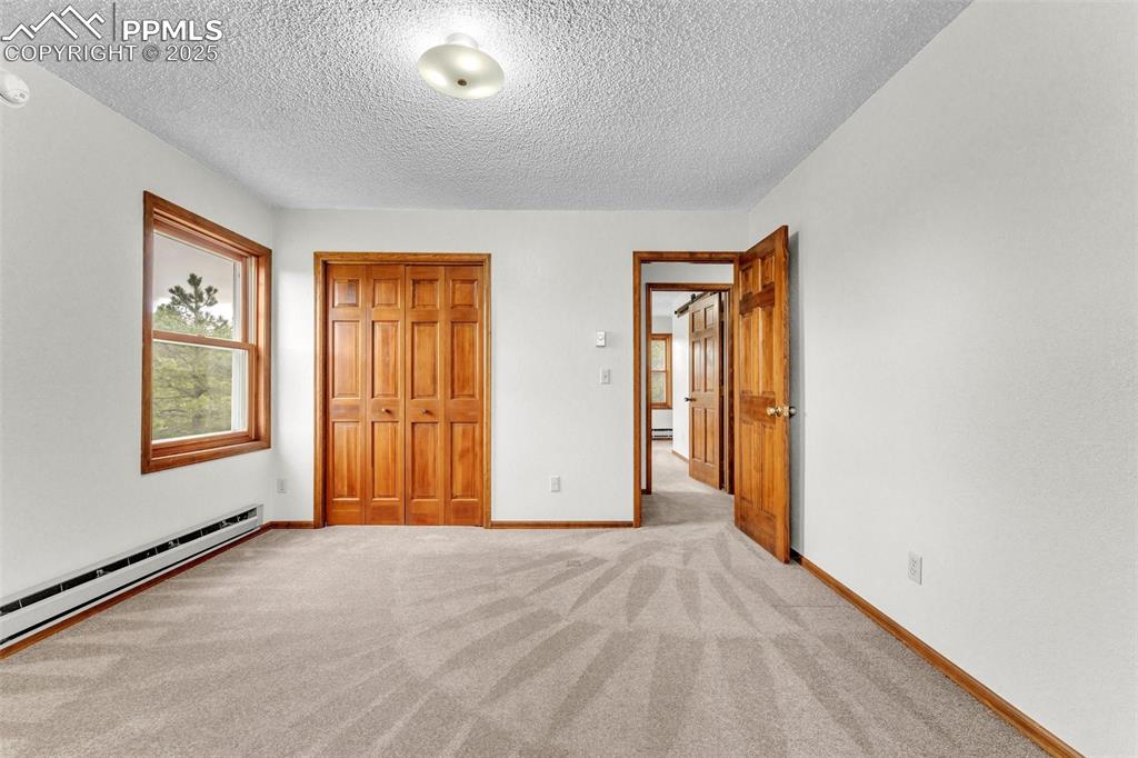 Image 22 of 43: Unfurnished bedroom featuring a closet, baseboard heating, a textured ceili