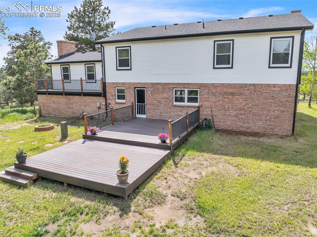 Image 24 of 43: Back of house featuring brick siding, a yard, a chimney, and a deck