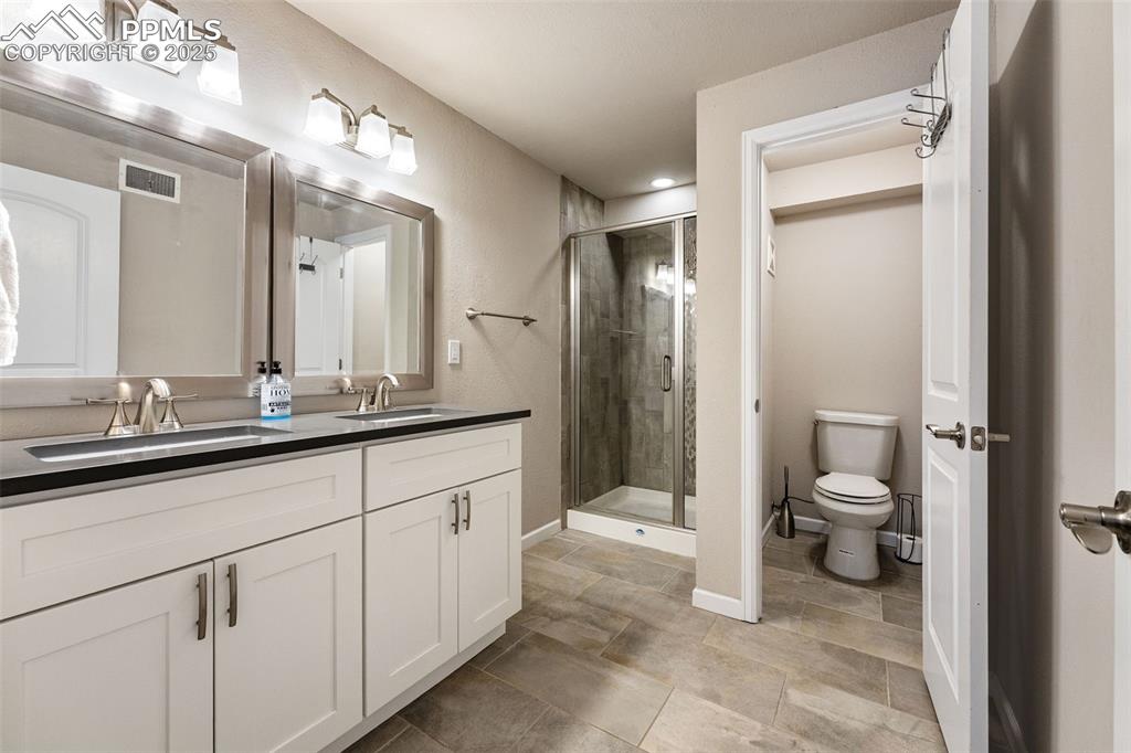 Image 12 of 29: Full bathroom with double vanity, a stall shower, and stone finish floors