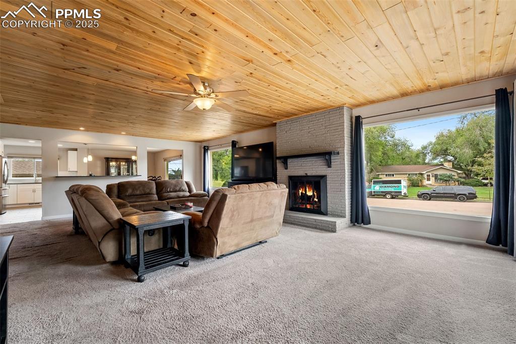 Image 3 of 29: Living area featuring carpet floors, wood ceiling, ceiling fan, and a firep