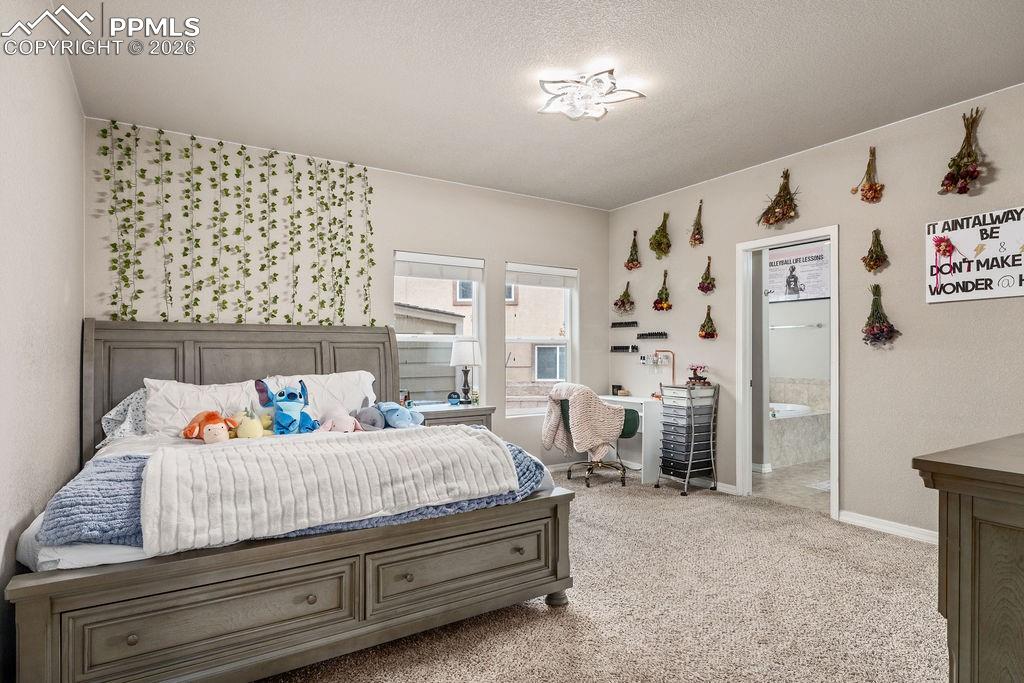 Image 16 of 43: Main floor primary bedroom featuring light colored carpet, a textured ceili