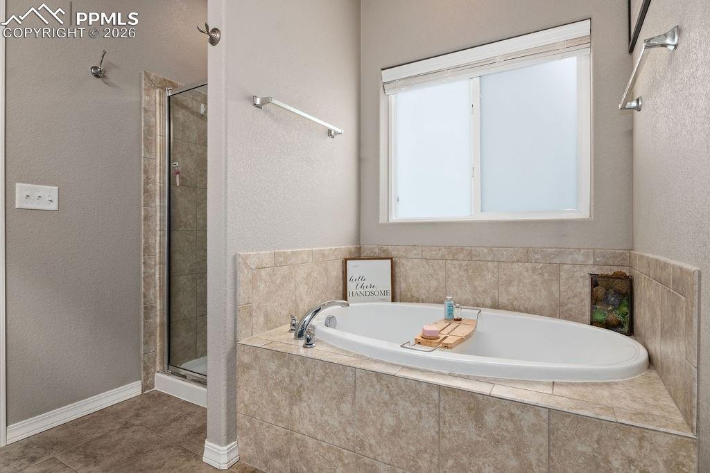 Image 18 of 43: Main floor primary bathroom featuring a stall shower, a bath, a textured wa