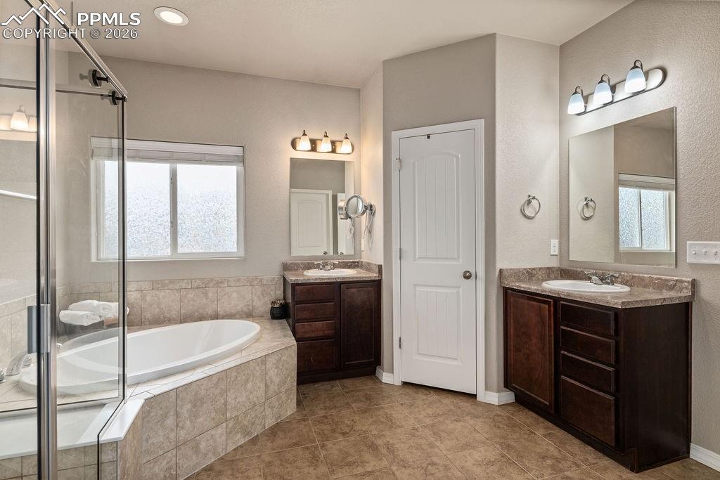Image 27 of 43: Full bathroom with two vanities, a bath, a shower stall, and light tile pat