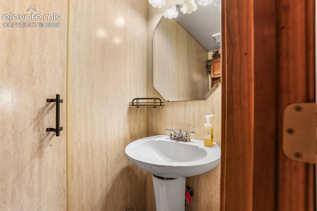 Image 28 of 33: Pedestal sink with chrome faucet, octagonal mirror, and wall-mounted light