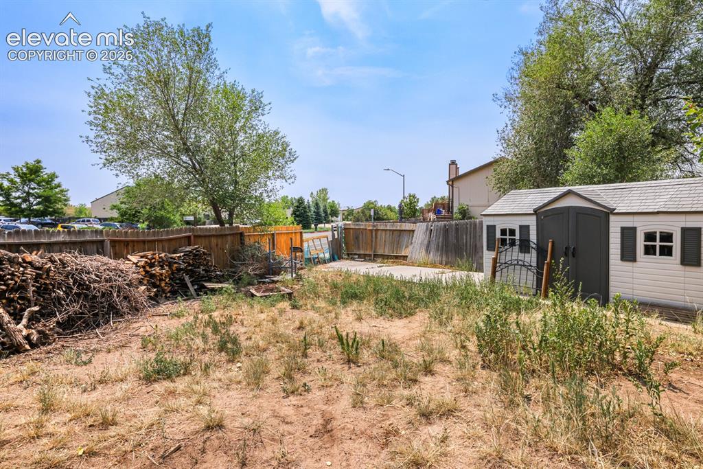 Image 29 of 33: Spacious backyard area featuring a wood fence, a large storage shed with fa