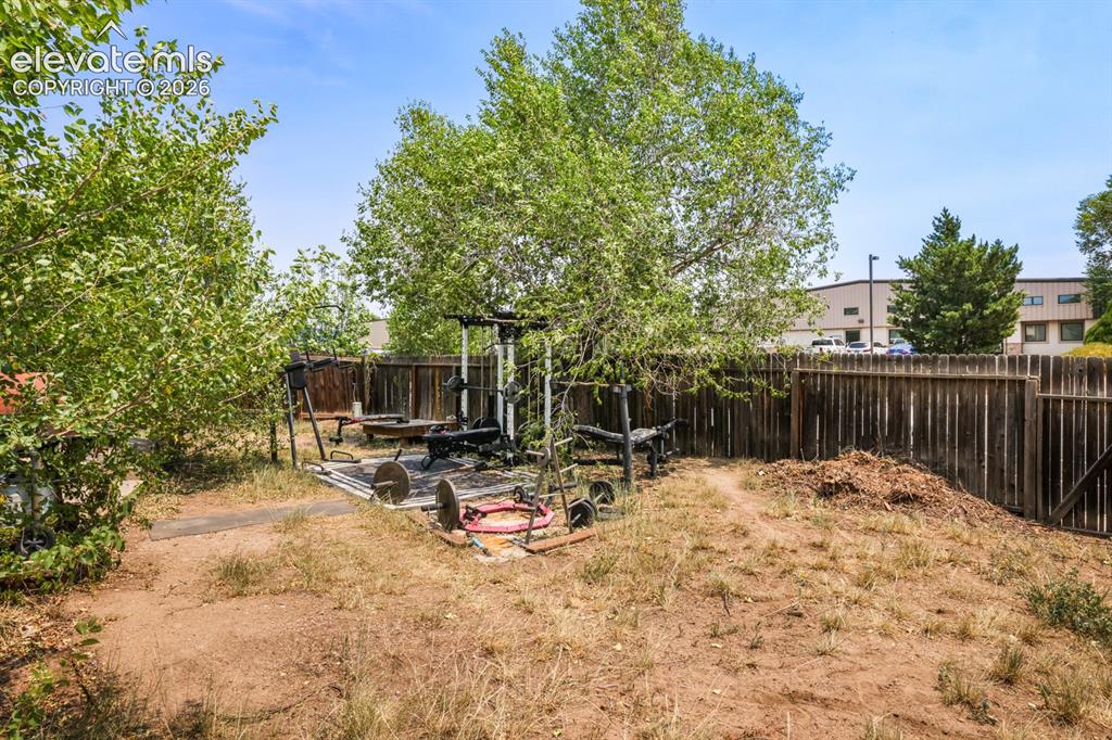 Image 30 of 33: Fenced backyard featuring mature trees and a dedicated paved area
