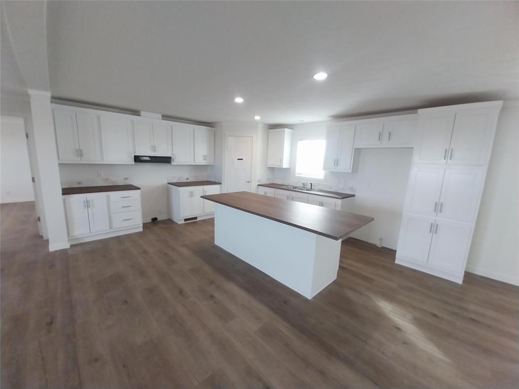 Image 17 of 28: Kitchen with white cabinetry, dark wood-type flooring, a center island, dar