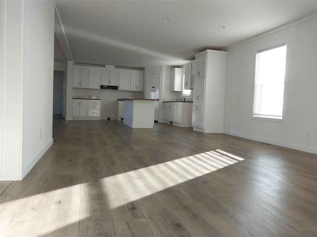 Image 24 of 28: Unfurnished living room with dark wood-style floors and baseboards