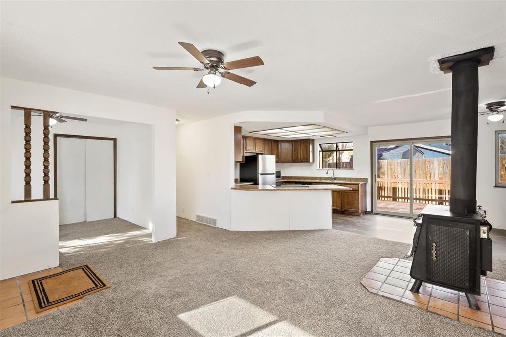 Image 5 of 32: Living room with view of kitchen and sliding glass door out to the wooden d
