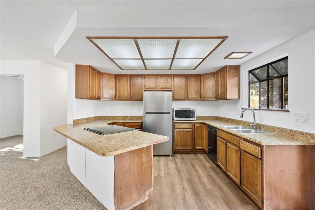 Image 7 of 32: Kitchen with brown cabinets, light countertops, and black appliances
