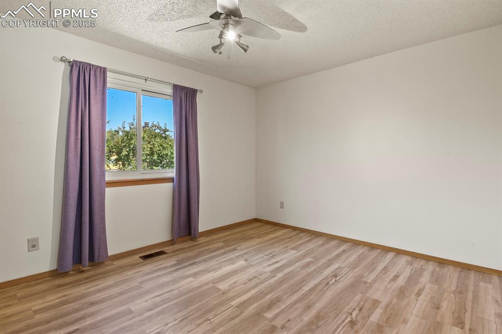 Image 16 of 30: Second bedroom featuring light wood-type flooring, ceiling fan, and a textu
