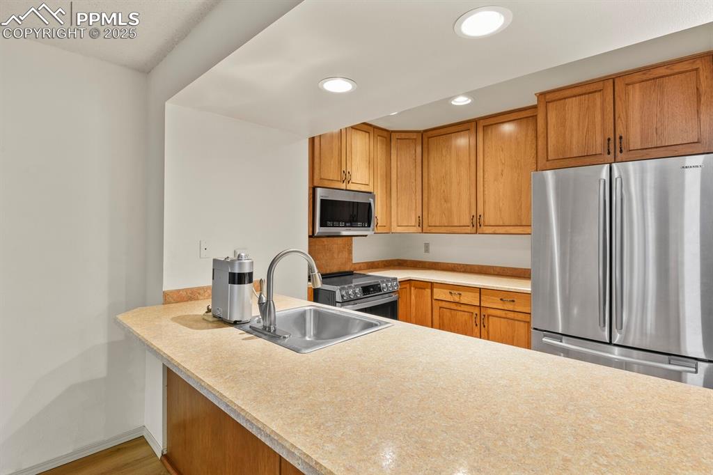 Image 6 of 30: Kitchen with stainless steel appliances, brown cabinetry, light countertops