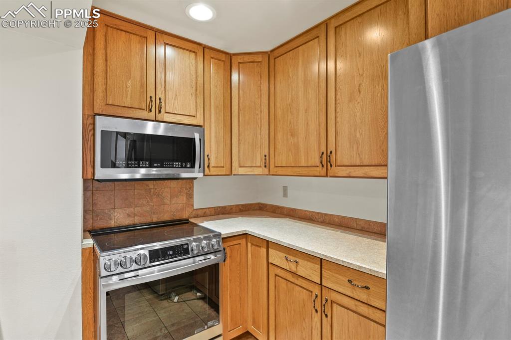 Image 8 of 30: Kitchen with stainless steel appliances, light countertops, backsplash, and