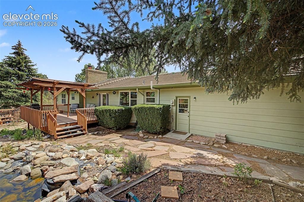 Image 35 of 43: The stone walkway, deck with pergola, and mature landscaping make this home