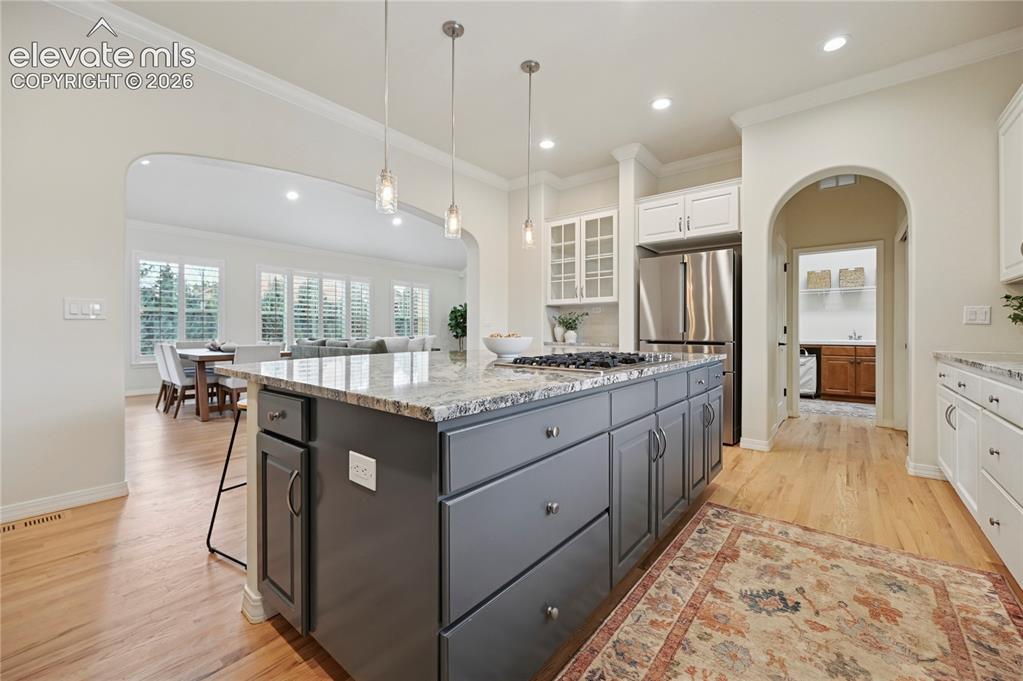 Image 10 of 49: Kitchen featuring arched walkways, two tone cabinets, light stone counters,