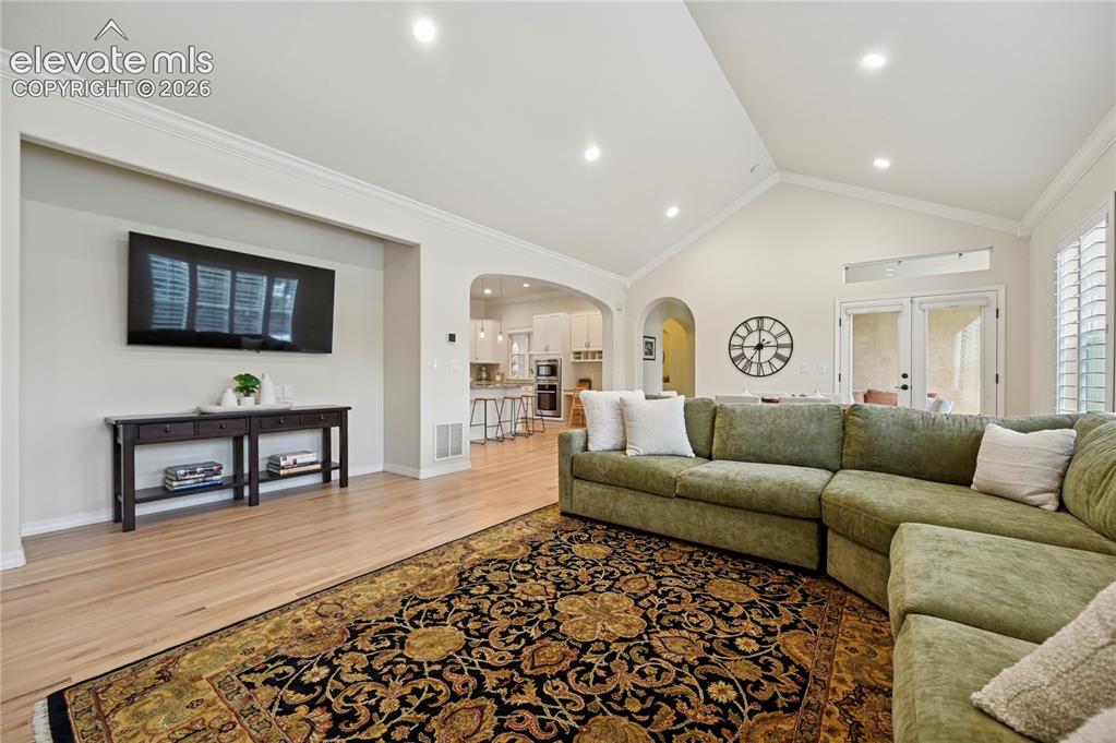 Image 14 of 49: Living area with arched walkways, light wood-style floors, ornamental moldi
